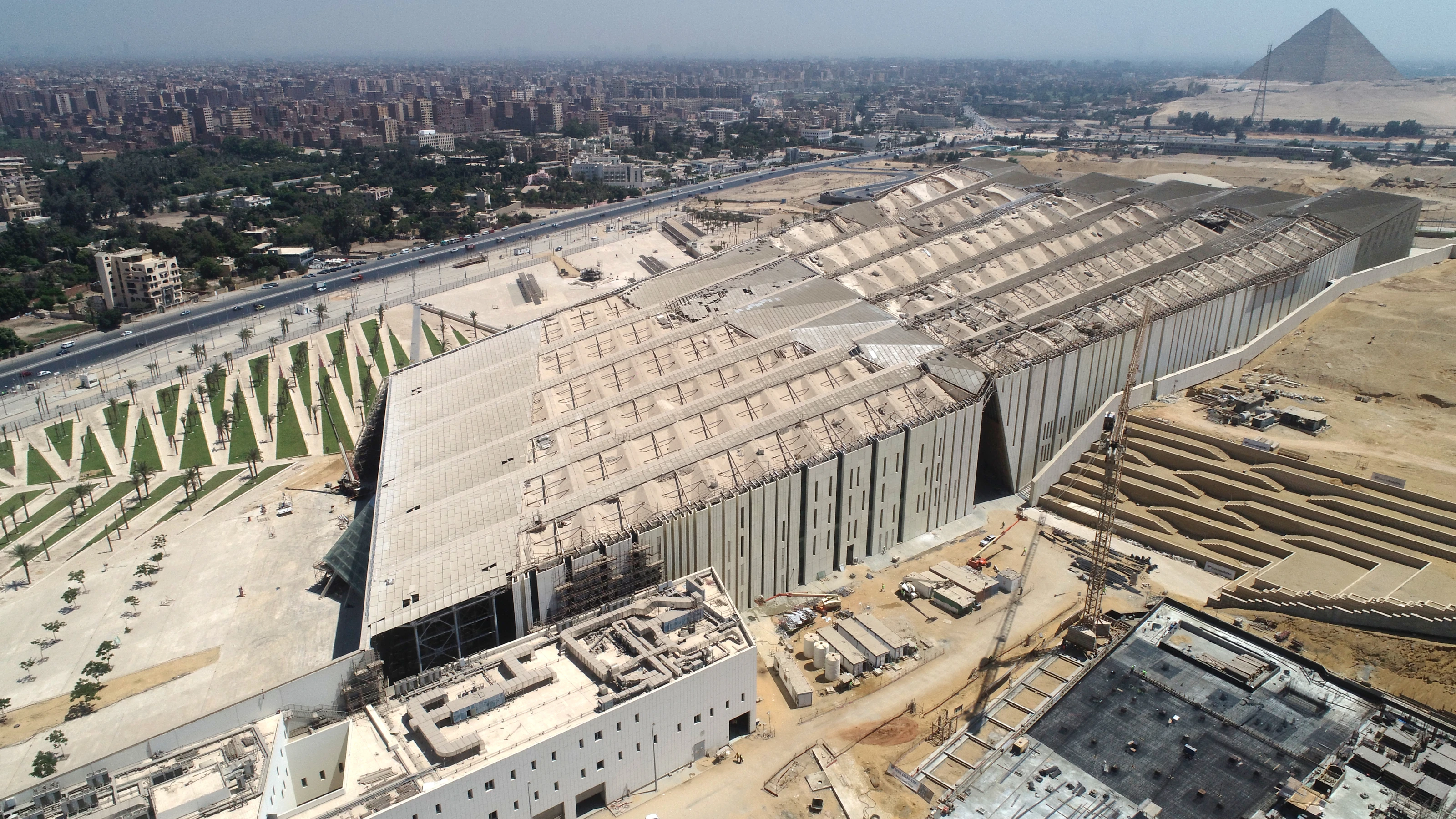 Wide aerial construction view of the Grand Egyptian Museum in Giza with the Great Pyramid beyond